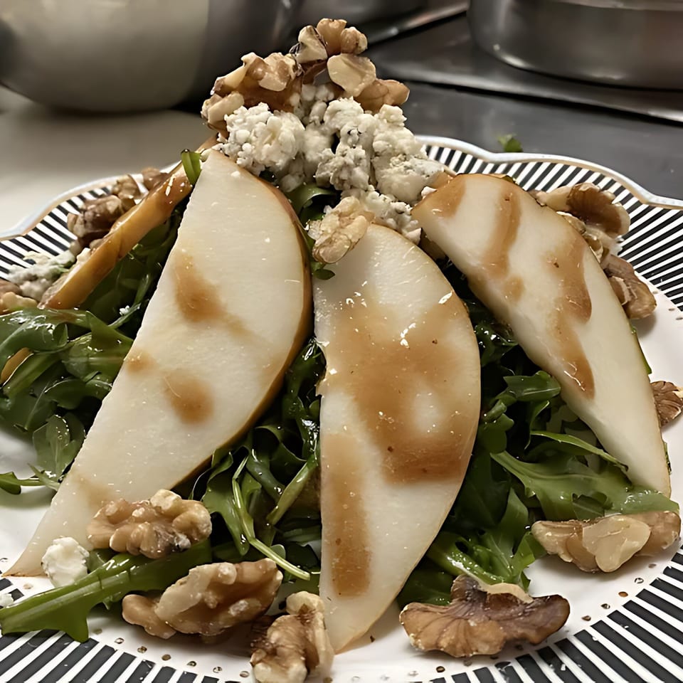 Arugula salad with sliced pears, crumbled blue cheese, and walnuts on a striped plate.