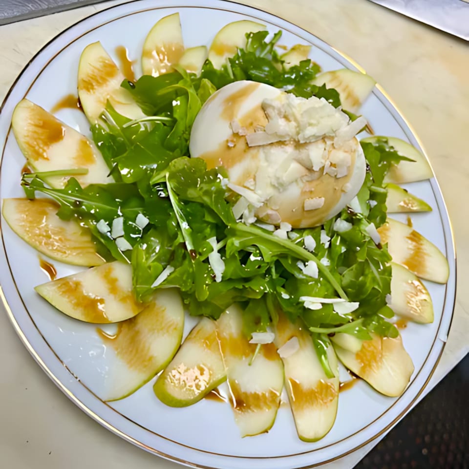Burrata cheese with arugula, sliced pears, balsamic glaze, and shaved parmesan on a white plate.